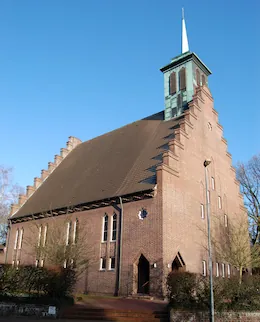 Rote Backsteinkirche mit spitzem Turm unter blauem Himmel.