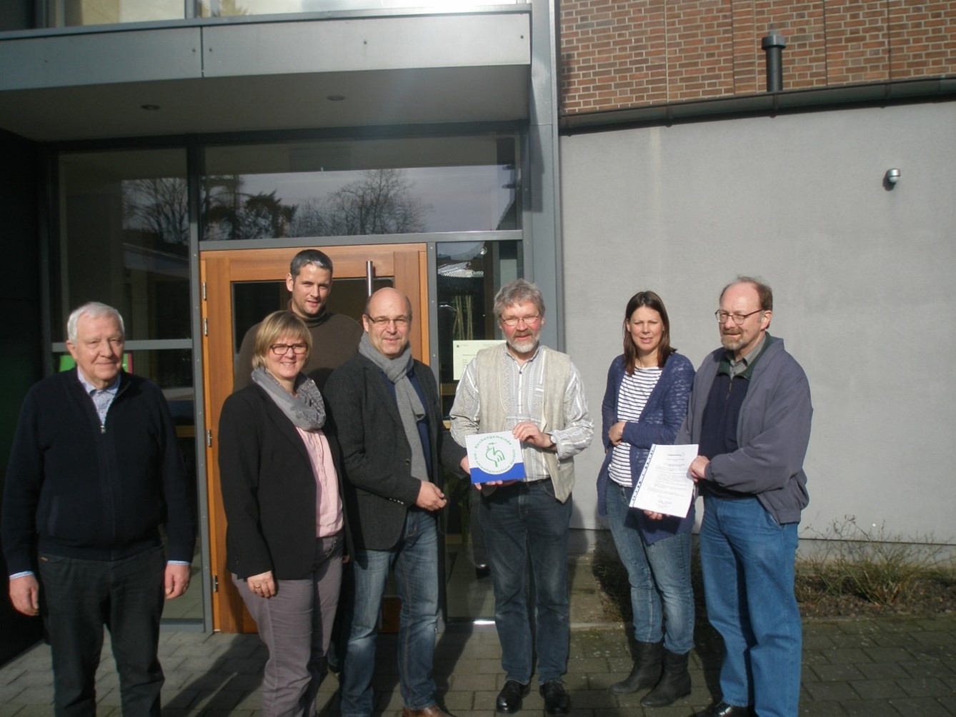 eine Gruppe von MEnschen dsteht vor einem Gebäude und hat eine Auszeichnung erhalten