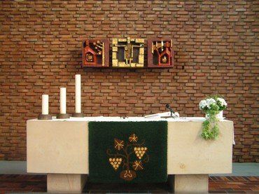 Kirchenaltar mit Kerzen, grüner Decke und Wandkunst.