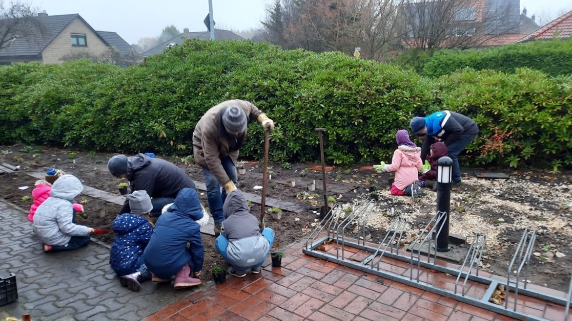 mehrere Kinder und zwei Erwachsene arbeiten im Garten