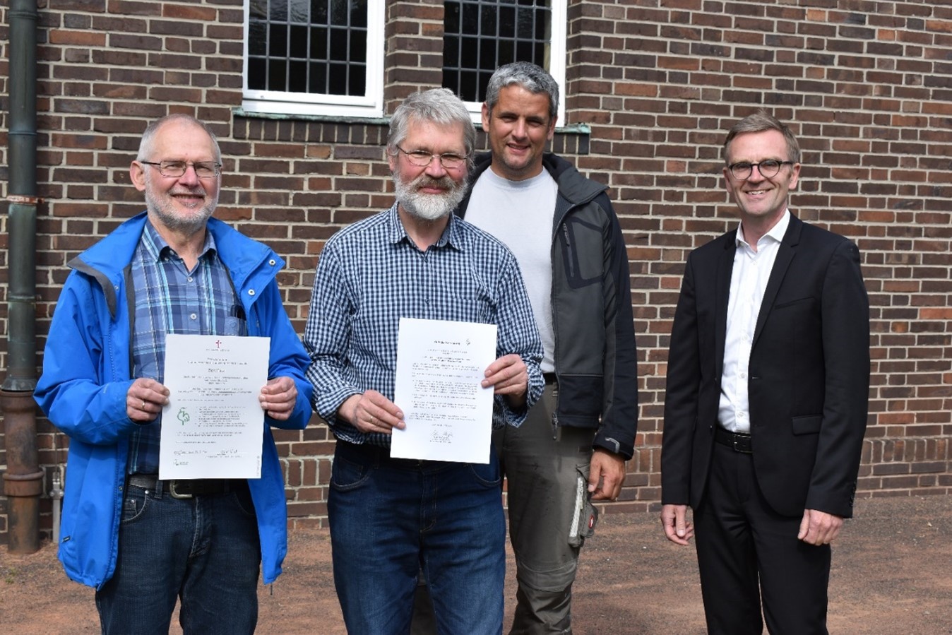 vier Menschen stehen vor einem Gebäude und haben eine Auszeichnung erhalten