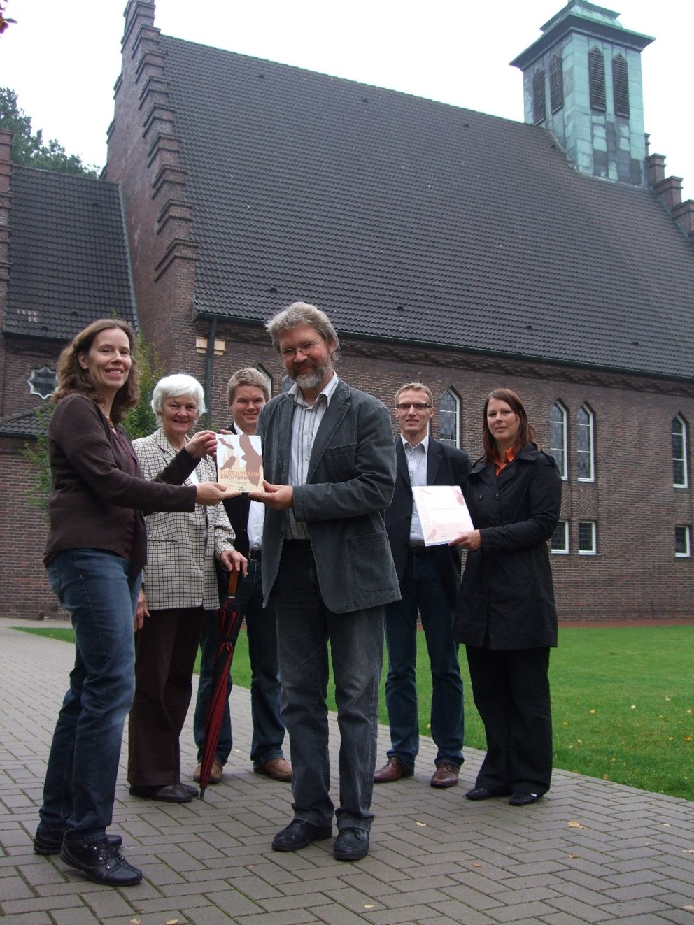 Verleihung einer Auszeichnung, sechs Menschen vor einer Kirche